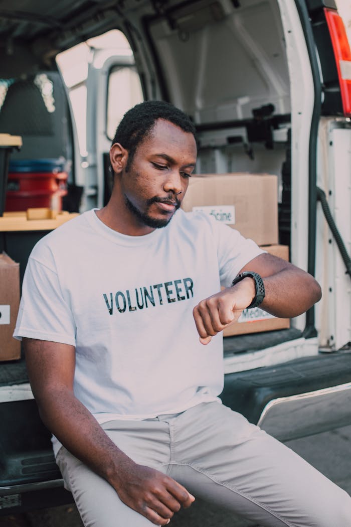 Home A volunteer sitting by a van, checking time, highlighting community service involvement.